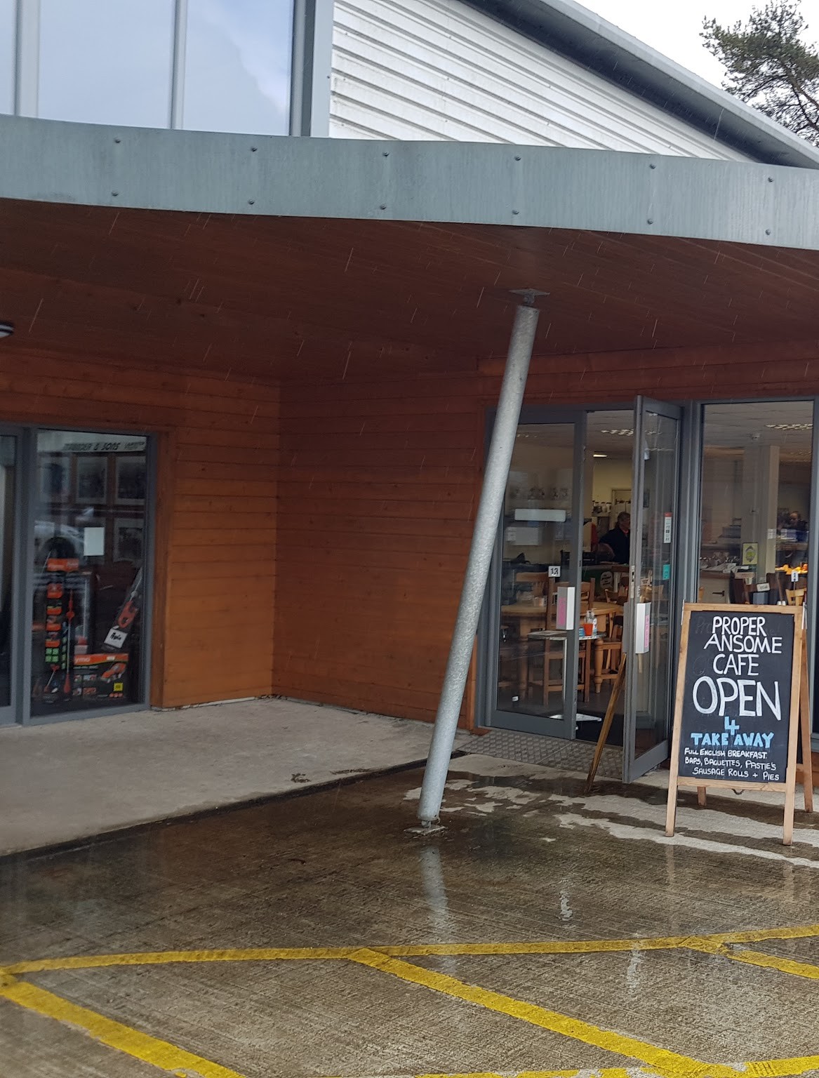 The café entrance under a curved timber canopy, with a chalk A-board reading Proper Ansome Cafe, open for takeaway