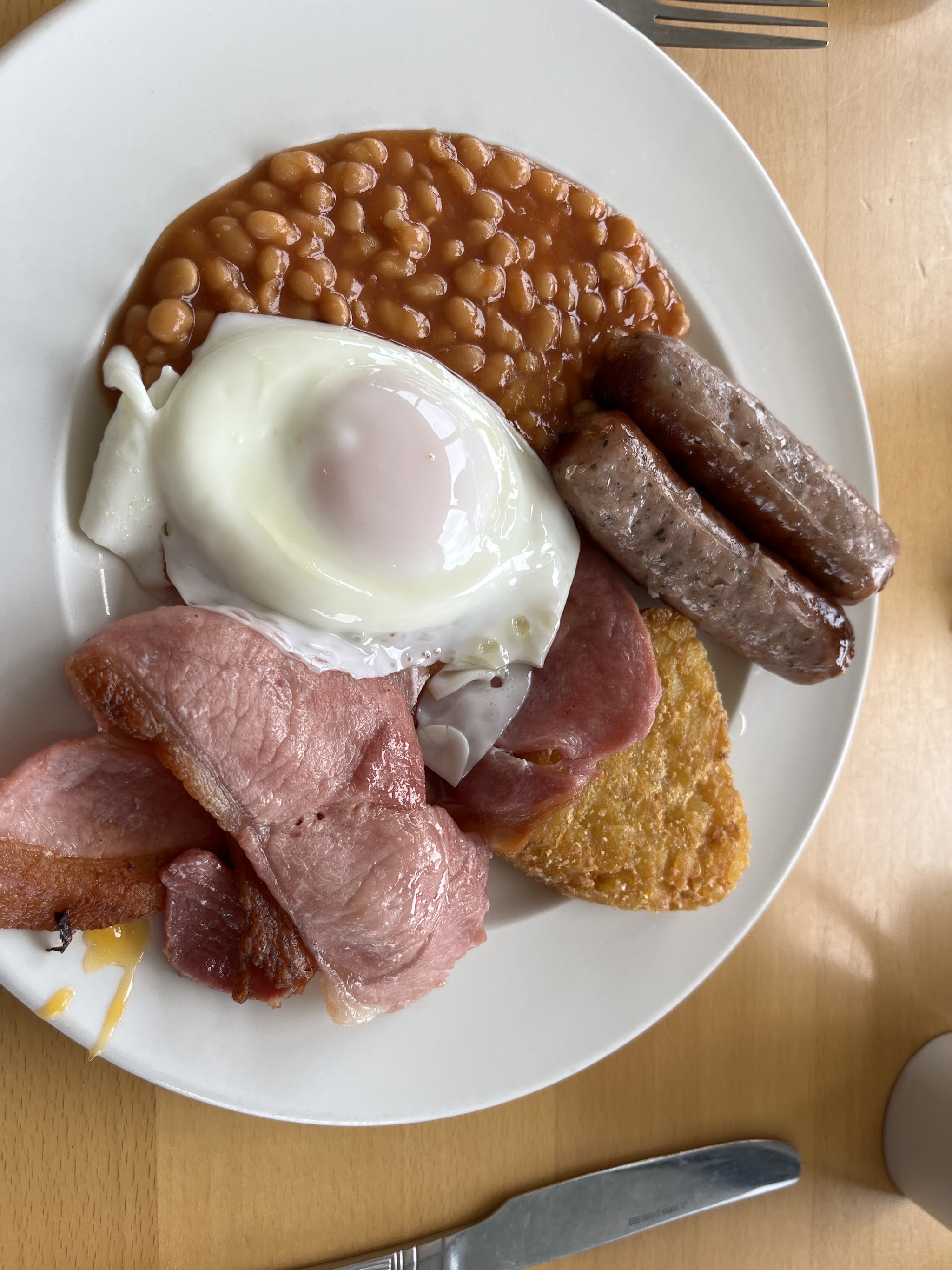 Breakfast plate with a fried egg, ham, two sausages, a hash brown and baked beans
